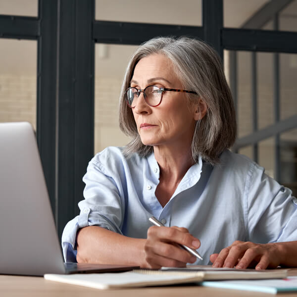 Woman sitting at desk writing while looking at the computer.