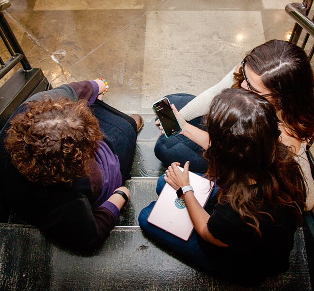 Tatum and team members sitting on steps reviewing social media content on smart phone