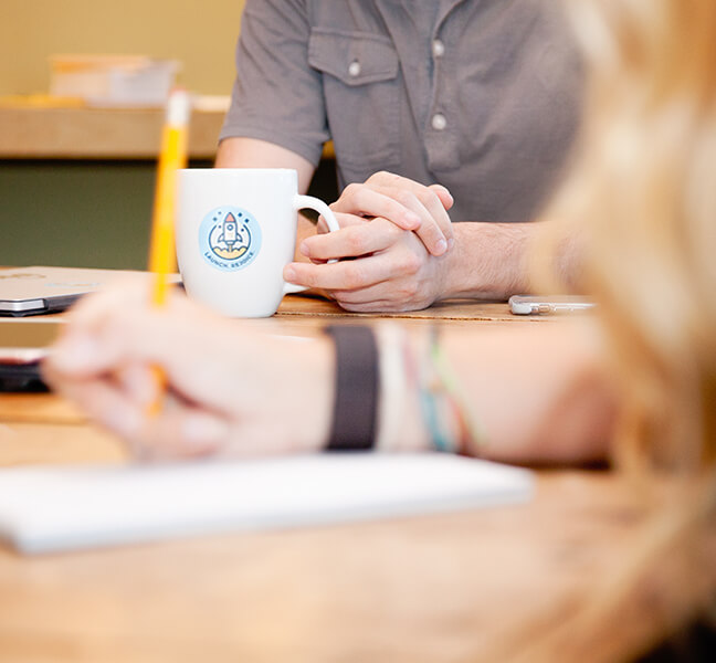 Close-up of hands holding coffee cup with TBH sticker in strategy meeting